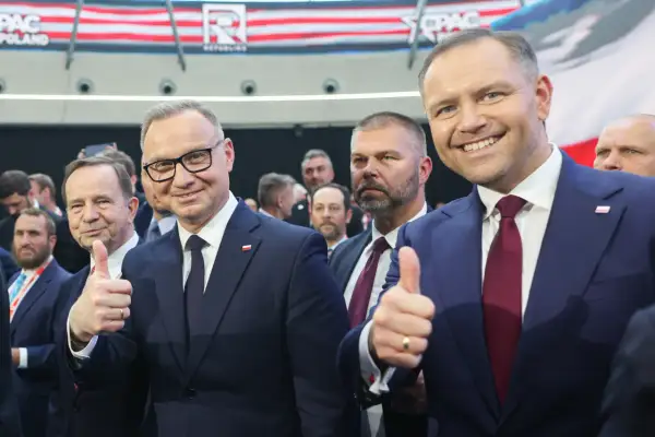 Dwóch mężczyzn w garniturach, jeden z nich pokazuje kciuk w górę. W tle widać napis CPAC Poland. Długość kadencji prezydenta jest tematem dyskusji.