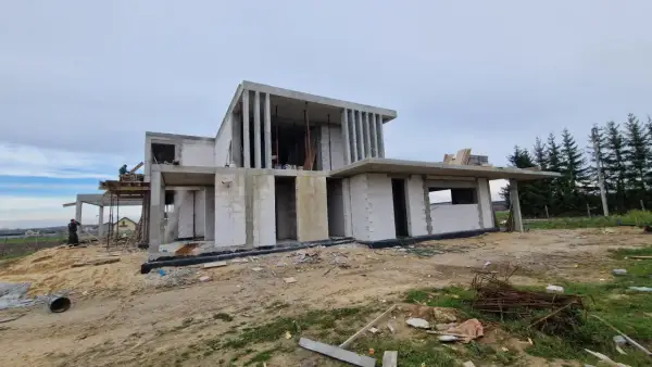 Budowa nowoczesnego domu z betonu i białych pustaków, w tle las.
