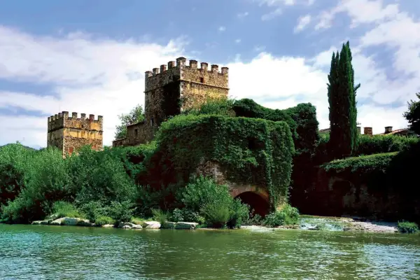Antiche gualchiere di Remole, torri medievali immerse nel verde, si specchiano in un fiume tranquillo sotto un cielo nuvoloso.