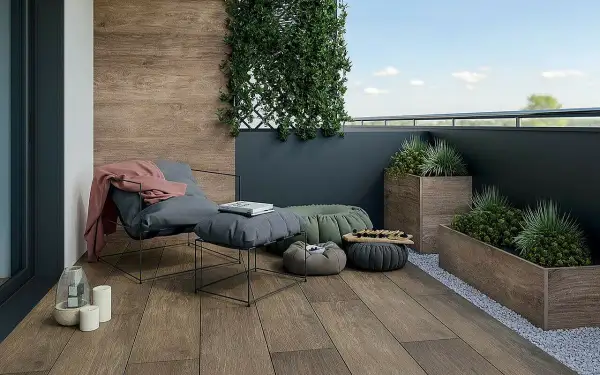 Drewnopodobne płytki na balkon tworzą przytulną atmosferę. Wygodny fotel, pufy i rośliny zapraszają do relaksu.