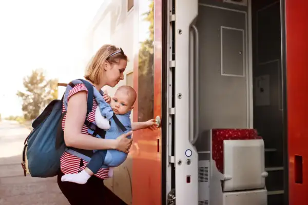 Frau mit Baby im Tragetuch steigt in den Zug. Abenteuerliches Backpacking mit Baby beginnt.