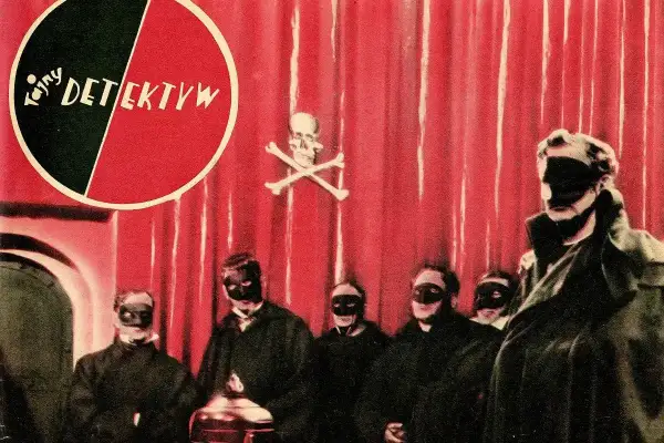 Grupa zamaskowanych postaci w czarnych strojach, na czerwonym tle z symbolem czaszki i piszczeli. Może to być scena z tajemniczej czarnej mszy.