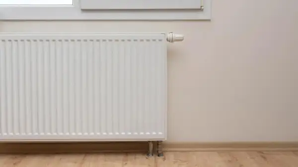 Biały grzejnik pod oknem, termostat ustawiony na 60 stopni, ale grzejniki letnie.