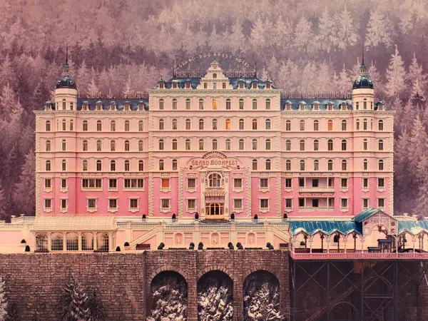 A grand pink hotel with a distinct Wes Anderson aesthetic, nestled in a snowy, purple-hued forest.