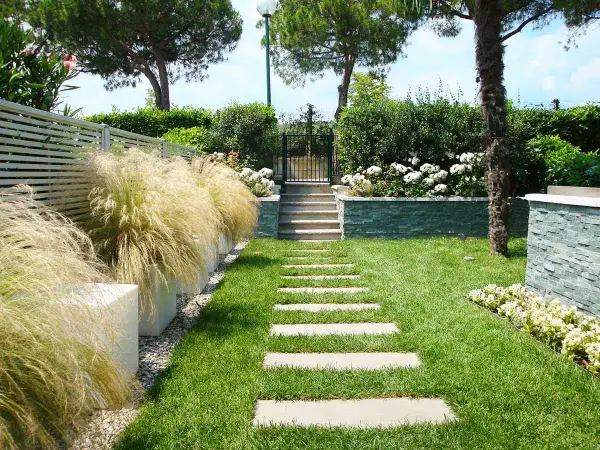 Un bellissimo giardino progetto con un sentiero di lastre di pietra, erba verde, cespugli fioriti e un muretto in pietra.
