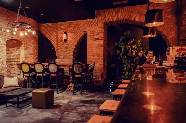 Ambiente acogedor en la praga vermuteria, con ladrillos expuestos, luces cálidas y cómodos asientos.
