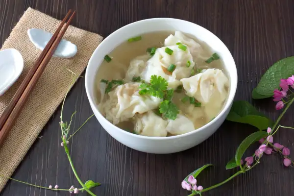 Aromaticzne chińskie pierożki w bulionie, ozdobione szczypiorkiem i kolendrą, gotowe do spożycia z pałeczkami.