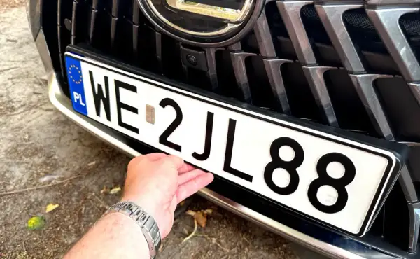 Dłoń poprawia tablicę rejestracyjną z numerem WE 2JL88, przygotowując wniosek o rejestrację pojazdu.