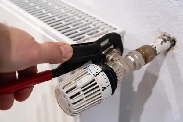 Hand uses pliers to heizungsventil tauschen. Der Thermostatkopf ist auf Stufe 3 eingestellt.