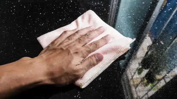 Mano limpiando manchas de humedad en mármol negro con un paño rosa.