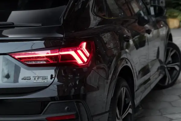 Czarne Audi Q3 45 TFSI quattro z zapalonymi światłami LED. Zbliżenie na tylną część pojazdu, podkreślające jego sportowy charakter i wymiary.