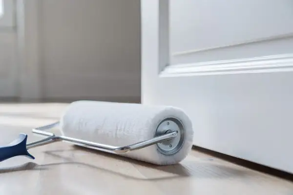 Rouleau de peinture blanc sur parquet, prêt à enlever traces rouleau de peinture sur une porte blanche.