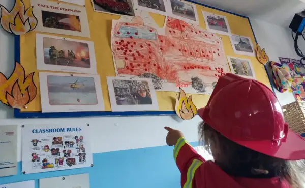 Niña con casco de bombero señala un mural de bomberos, parte de originales proyectos infantiles.