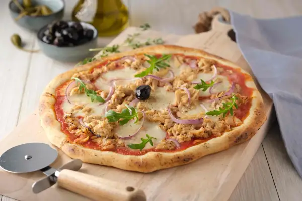 Une délicieuse pizza au thon, garnie de mozzarella fondante, d'oignons rouges et de roquette fraîche, prête à être découpée.