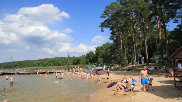 Słoneczny dzień nad jeziorem w Augustowie. Ludzie kąpią się, opalają na plaży i spacerują po molo.