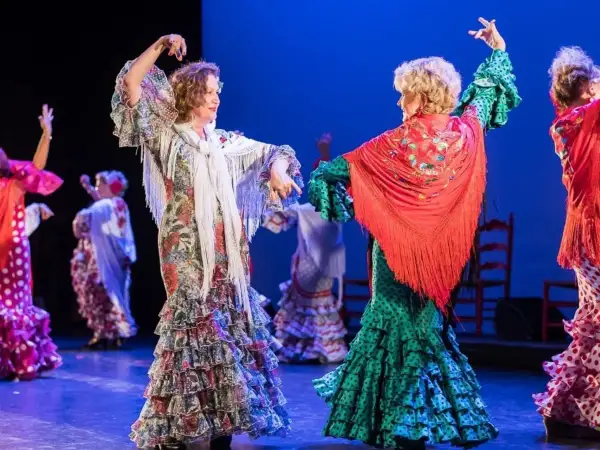 Dos mujeres bailan sevillanas, con volantes y mantones, evocando el origen de esta danza.