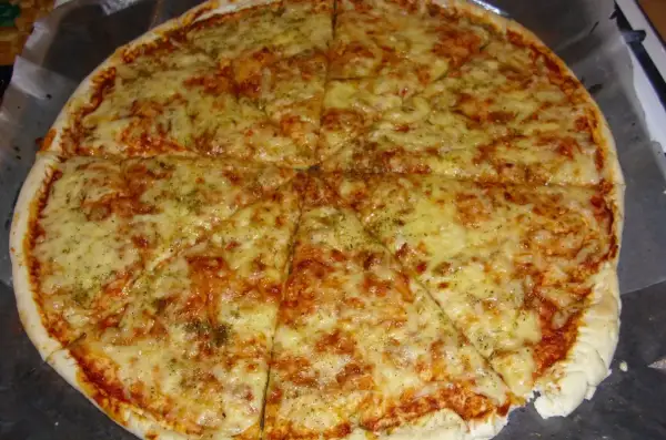 Pyszna, gorąca margarita pizza z ciągnącym się serem i aromatycznymi ziołami, pokrojona na 8 kawałków.