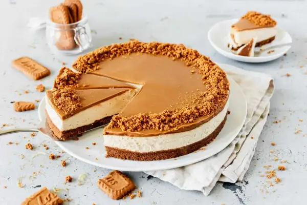 Ein köstlicher Lotus Cheesecake mit Karamellglasur und Keksbröseln. Ein Stück wurde bereits entnommen.