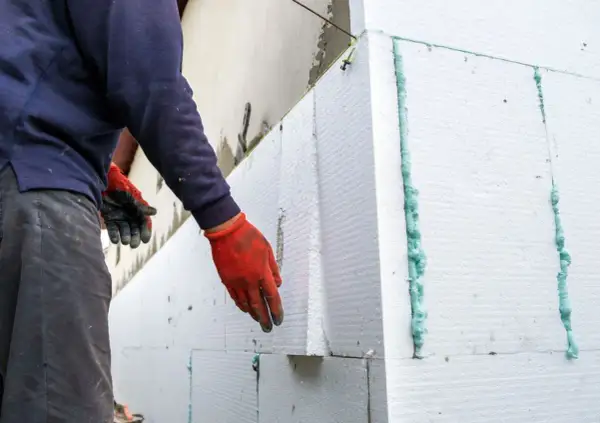 Operaio con guanti rossi applica pannelli per cappotto termico su intonaco esistente.