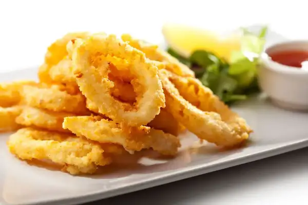 Anelli di totano dorati e croccanti, cotti in friggitrice ad aria, serviti su un piatto bianco con contorno di insalata e salsa.
