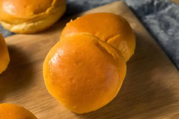 Pains à burger maison dorés et moelleux sur une planche en bois.