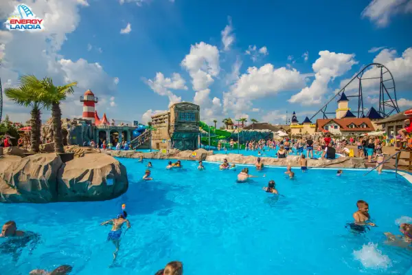 Energylandia wodne atrakcje: ludzie kąpią się w basenie, zjeżdżalnie i roller coaster w tle.