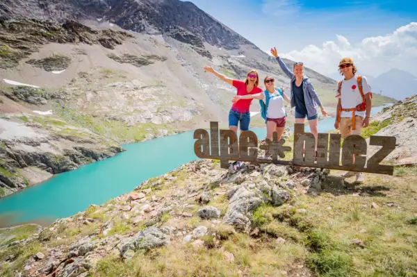 Quatre amis profitent de leurs vacances d'été dans les Alpes, près d'un lac turquoise. Ils posent devant un panneau "alpe d'huez".