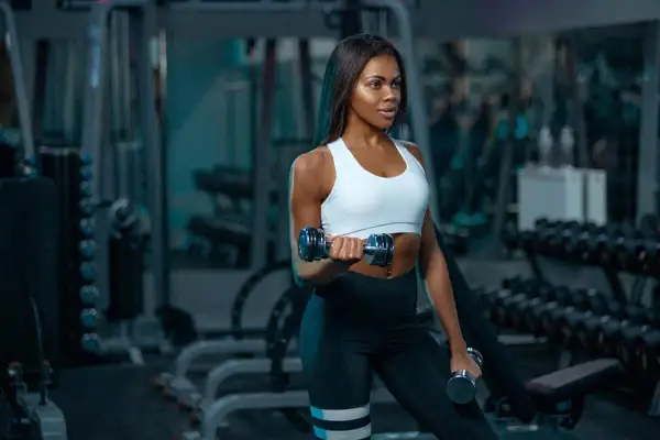 A woman with muscular arms lifts dumbbells in a gym, showcasing her dedication to fitness.