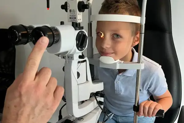 Chłopiec podczas badania okulistycznego. Lekarz sprawdza reakcję źrenic na światło, co może pomóc w diagnostyce.