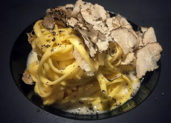Tagliatelle al tartufo, un piatto elegante con pasta fresca condita con una cremosa salsa e generosamente guarnita con scaglie di tartufo nero.