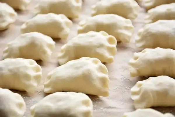 Gotowe do gotowania ciasto na pierogi, ułożone rzędami na blacie.
