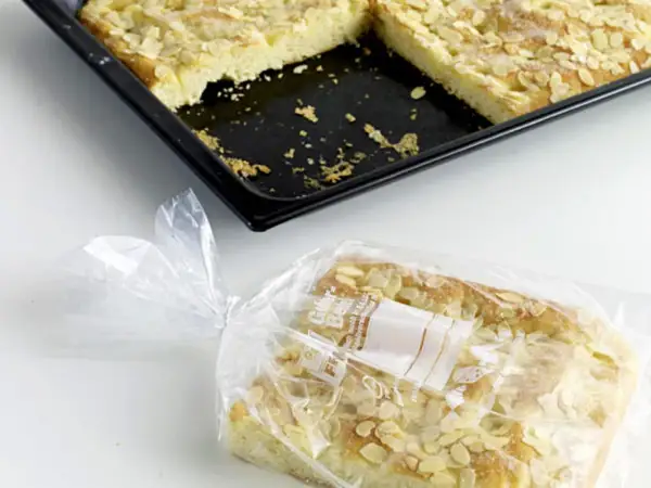 Ein Stück Mandelkuchen ist in einer Plastiktüte verpackt, bereit zum Kuchen einfrieren. Daneben liegt die Backform mit den restlichen Stücken.