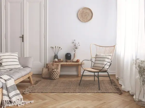 Un angolo del salotto arredato con un divanetto in legno, una poltrona in rattan, tappeto in juta e decorazioni naturali. Ecco come riempire un angolo del salotto con stile.