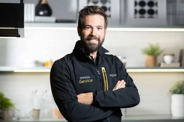 Uśmiechnięty serwisant Whirlpool w czarnej kurtce z napisem "Official Service". Pomoże Ci z instrukcją obsługi pralki Whirlpool.