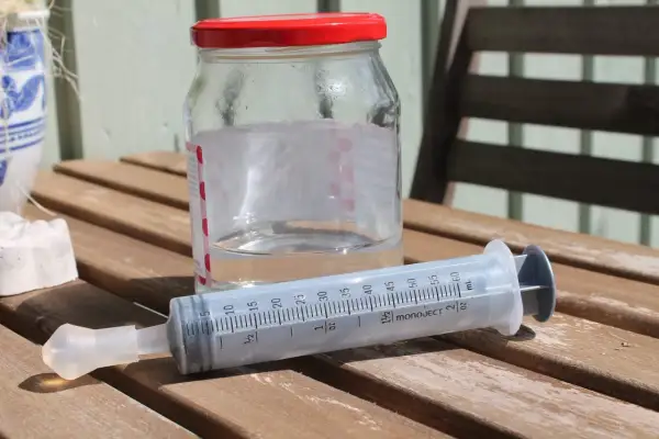 En spruta med koksaltlösning för barn står bredvid ett glas med vatten.