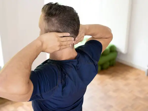 Mann mit Händen im Nacken, der sich fragt: nackenschmerzen wann zum arzt.