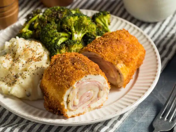 Un delicioso cordon bleu, crujiente por fuera y jugoso por dentro, acompañado de puré de patatas y brócoli.