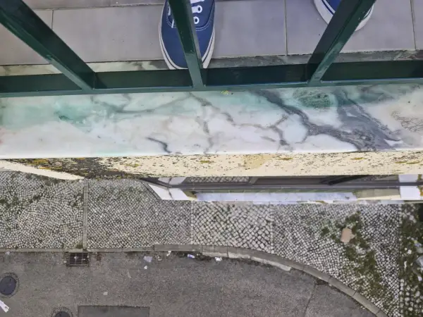 Come togliere la vernice dal marmo: una macchia verde su un davanzale di marmo, con scarpe blu in primo piano.