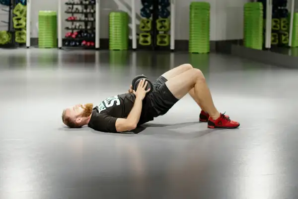 Mężczyzna z brodą wykonuje ćwiczenie glute bridge z obciążeniem na biodrach.