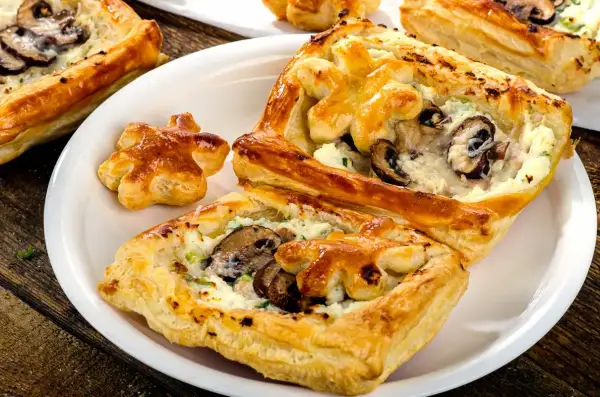 Chrupiące ciasto francuskie z pieczarkami i serem, podane na białym talerzu. Idealne na przekąskę.