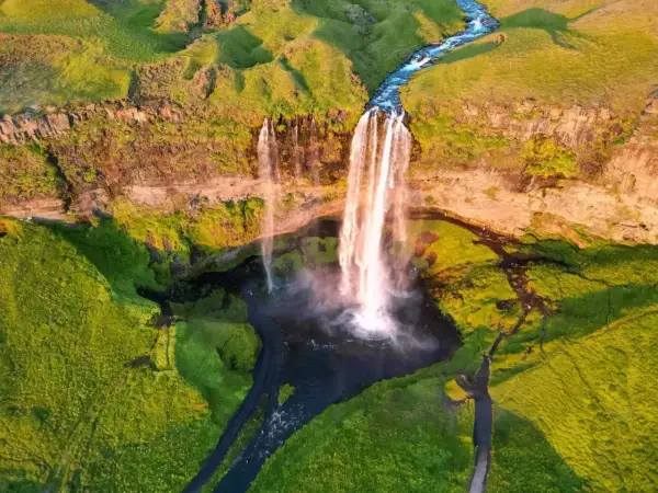 Wspaniały wodospad na Islandii latem. Zielone wzgórza i rwąca rzeka tworzą malowniczy krajobraz. Idealne miejsce, by zobaczyć, co Islandia ma do zaoferowania.
