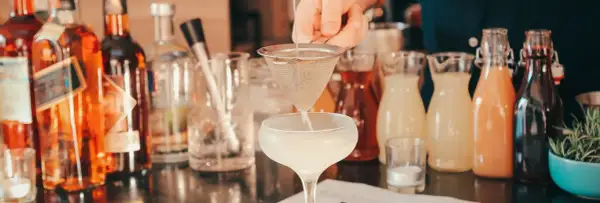 Barman przygotowuje drinka, obok stoją butelki z różnymi alkoholami i syropami. Idealny wybór, jaki alkohol na wesele, by zadowolić wszystkich gości.