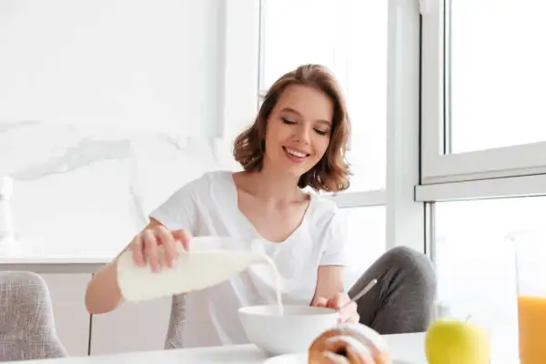 Uśmiechnięta dziewczyna nalewa mleko do miski, dbając o swoją masę kostną. Na stole croissant i jabłko.