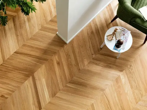 Un elegante parquet a spina di pesce, con un tavolino bianco e una poltrona verde. Per mantenere la sua bellezza, chiediti ogni quanto lavare il parquet.