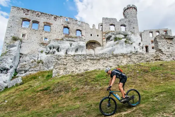 Rowerzysta pokonuje wzgórze na tle ruin zamku na Szlaku Orlich Gniazd.