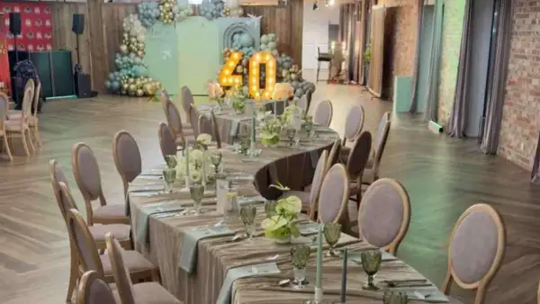 Eleganckie przyjęcie weselne na 40 osób. Stoły nakryte, ozdobione kwiatami i świecami. W tle dekoracje z balonów i podświetlana liczba 40.