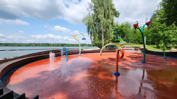 Kolorowy plac zabaw wodnych przy Jeziorze Paprocany, z fontannami i tęczą, zaprasza do zabawy w upalny dzień.