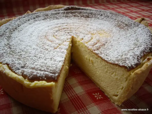 Une délicieuse tarte au fromage blanc, saupoudrée de sucre glace, prête à être dégustée sur une nappe à carreaux rouges.