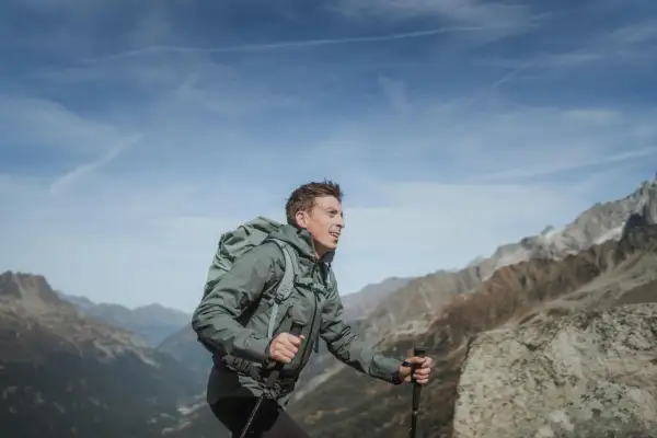 Mężczyzna z plecakiem i kijkami trekkingowymi wędruje po górach, podziwiając widok na masyw Mount Blanc.