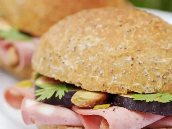 Un délicieux sandwich mortadelle garni de tranches d'aubergine, de pistaches et de persil frais, prêt à être dégusté.